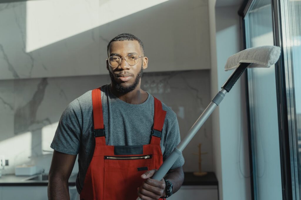 A professional cleaner holding a tool indoors, dressed in red overalls with natural light.